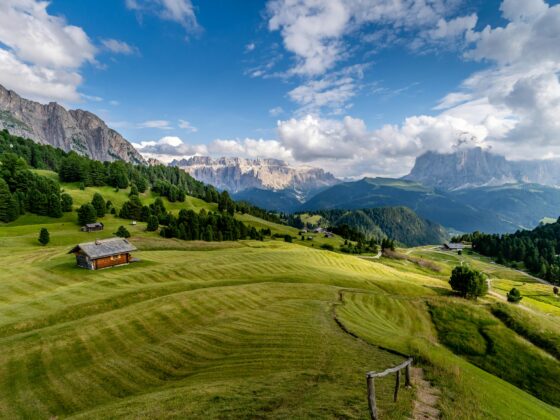 Green grass and fields with cabin. tall mountains and plump clouds in a blue sky