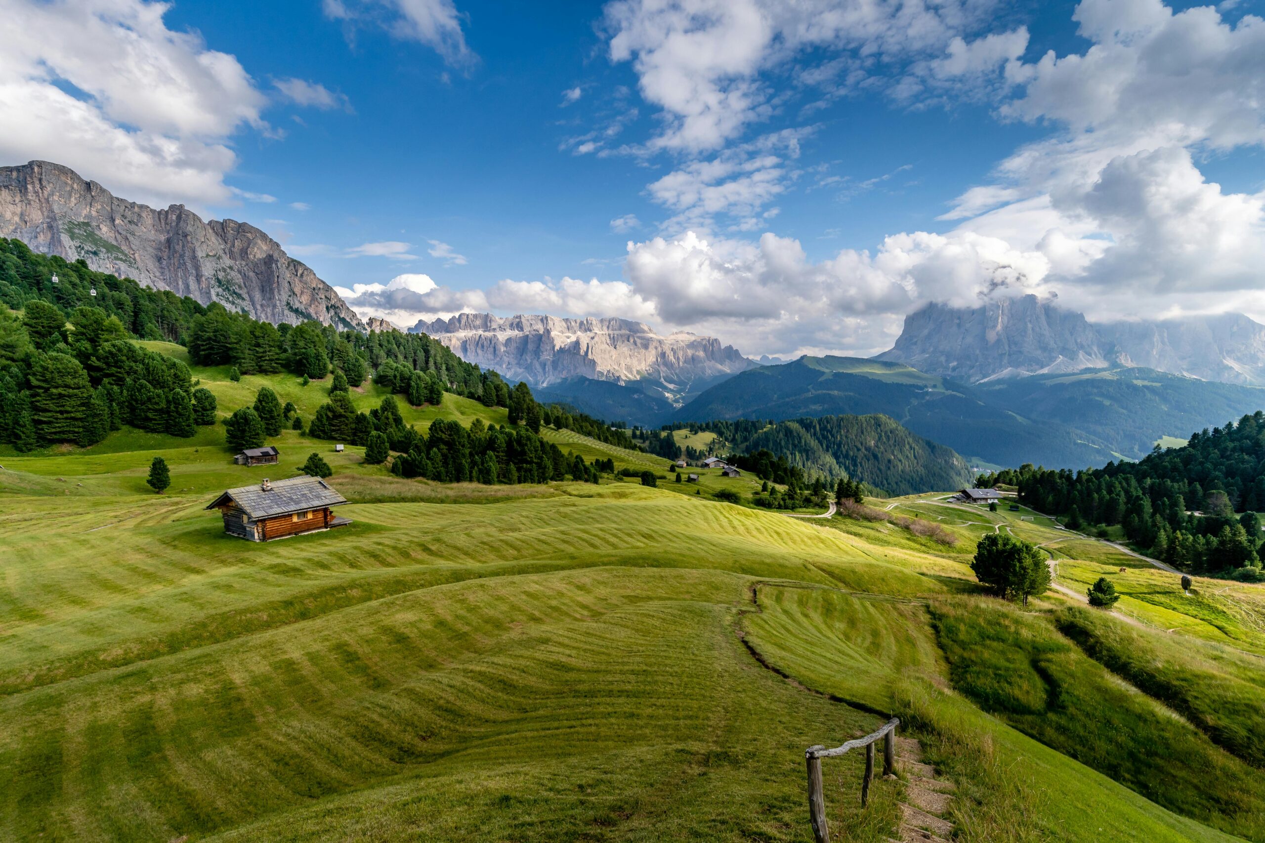 Green grass and fields with cabin. tall mountains and plump clouds in a blue sky